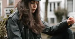 Lederjacke Frühling Outfit: Dame mit beiger Bikerjacke und weißem Kleid im Sonnenlicht.