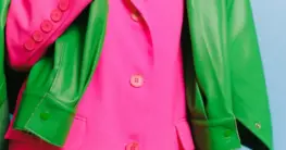 Lederjacke Statement Farbe in leuchtendem Rot, lässig über eine Schulter gelegt, vor urbanem Hintergrund.