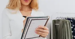 Lederjacke Lagerung Checkliste: Eine gut gepflegte schwarze Lederjacke hängt auf einem breiten Holzbügel in einem dunklen Kleiderschrank.
